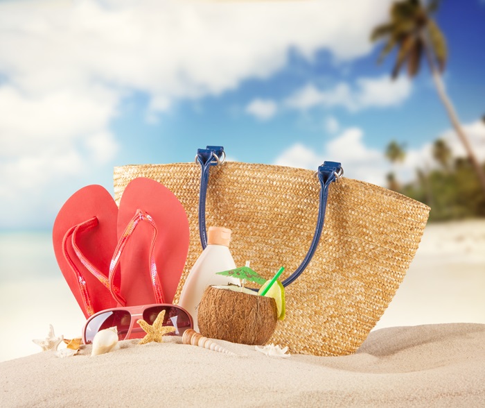 Un gros sac de plage sur du sable à la plage avec des chaussures, une boisson et des verres de plages